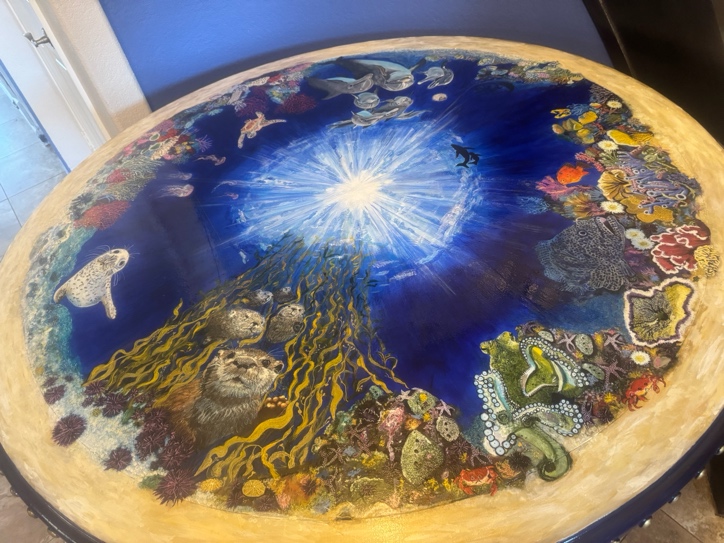 Hand-painted underwater scene on a round tabletop, with marine life surrounding a luminous sun