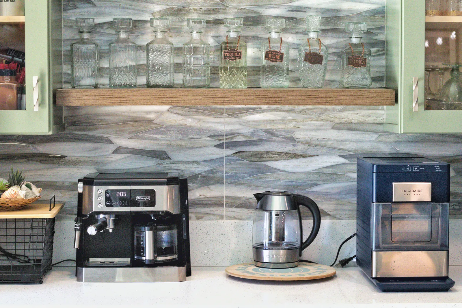 Glass wave-tile backsplash behind a floating wood shelf lined with labelled glass spirit decanters
