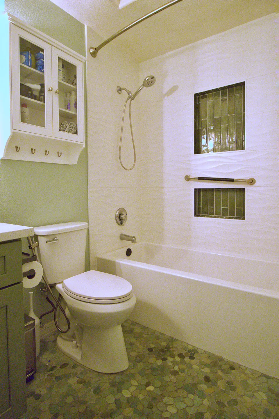 Sage green bathroom with a pebble mosaic floor and glass mosaic shower niches