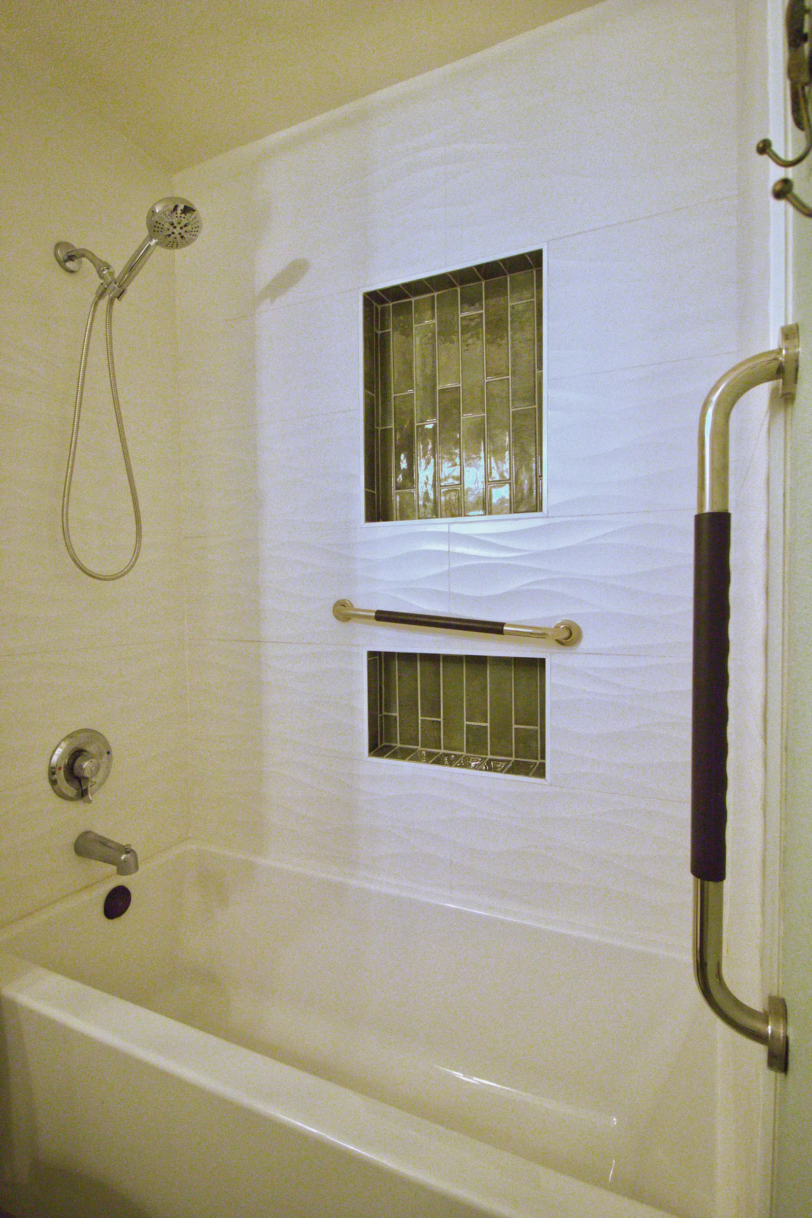 Tub and shower with a handheld sprayer, a horizontal grab bar and two recessed niches lined in green glass mosaic tile