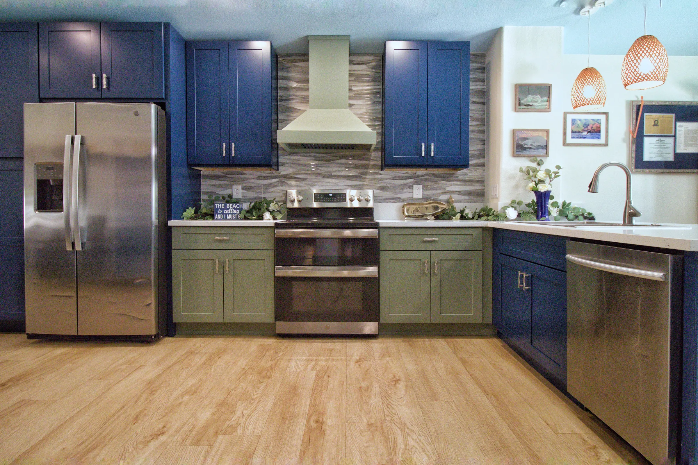 Coastal kitchen with navy upper cabinets, sage green lowers, a sage range hood and a gray glass wave-tile backsplash