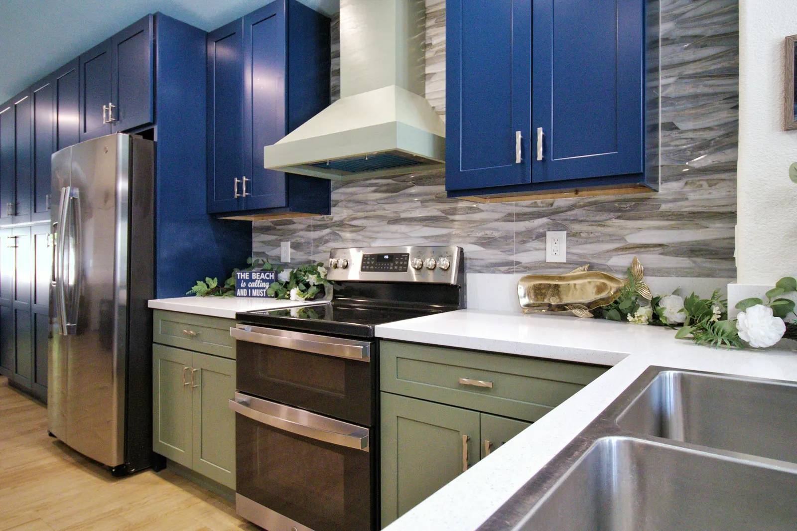 Slide-in range above a stainless double drawer oven, set between sage green lower cabinets