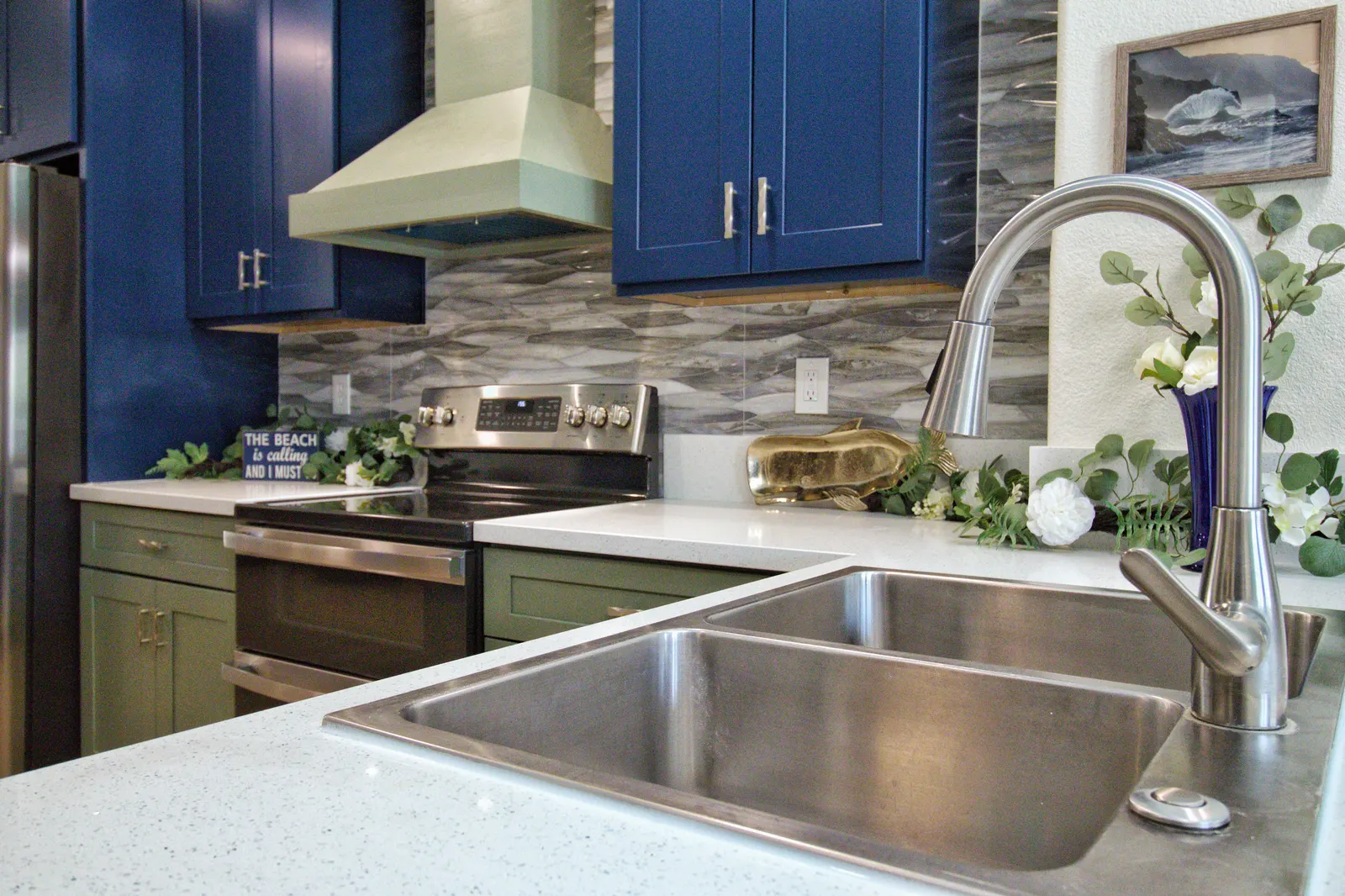 Stainless double-basin sink and pull-down faucet in white speckled quartz, with the glass wave backsplash behind