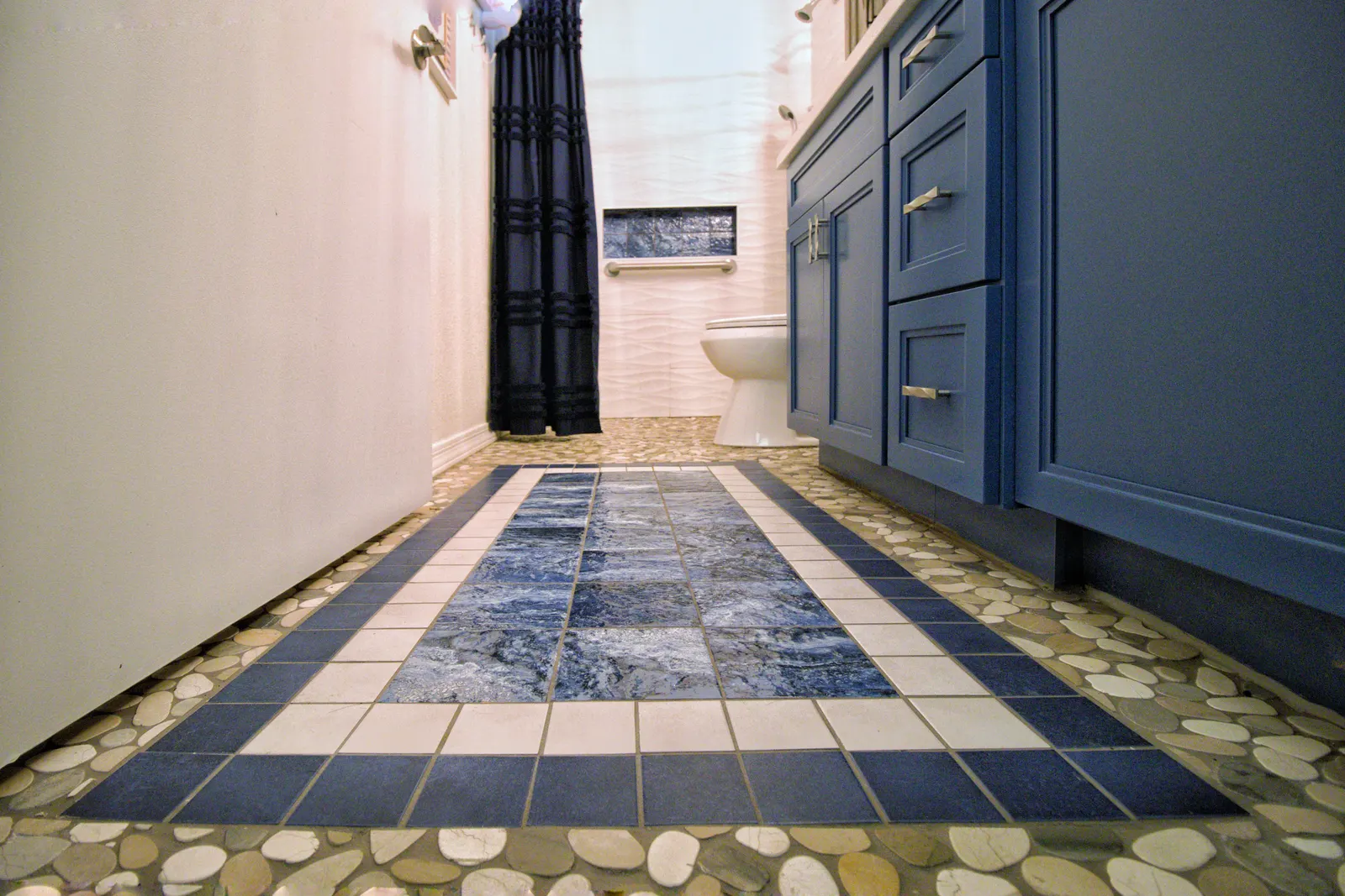 Bathroom floor detail: a rectangular inset of slate and stone tile bordered in cream, surrounded by river pebble mosaic