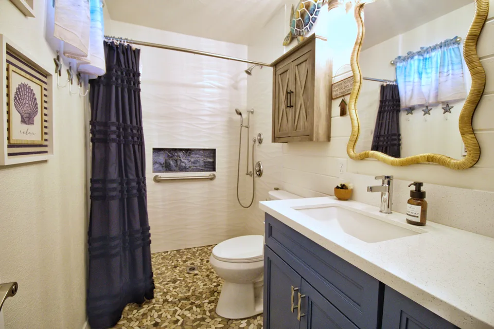 Bathroom with a navy vanity, a rattan-framed mirror and a pebble tile floor