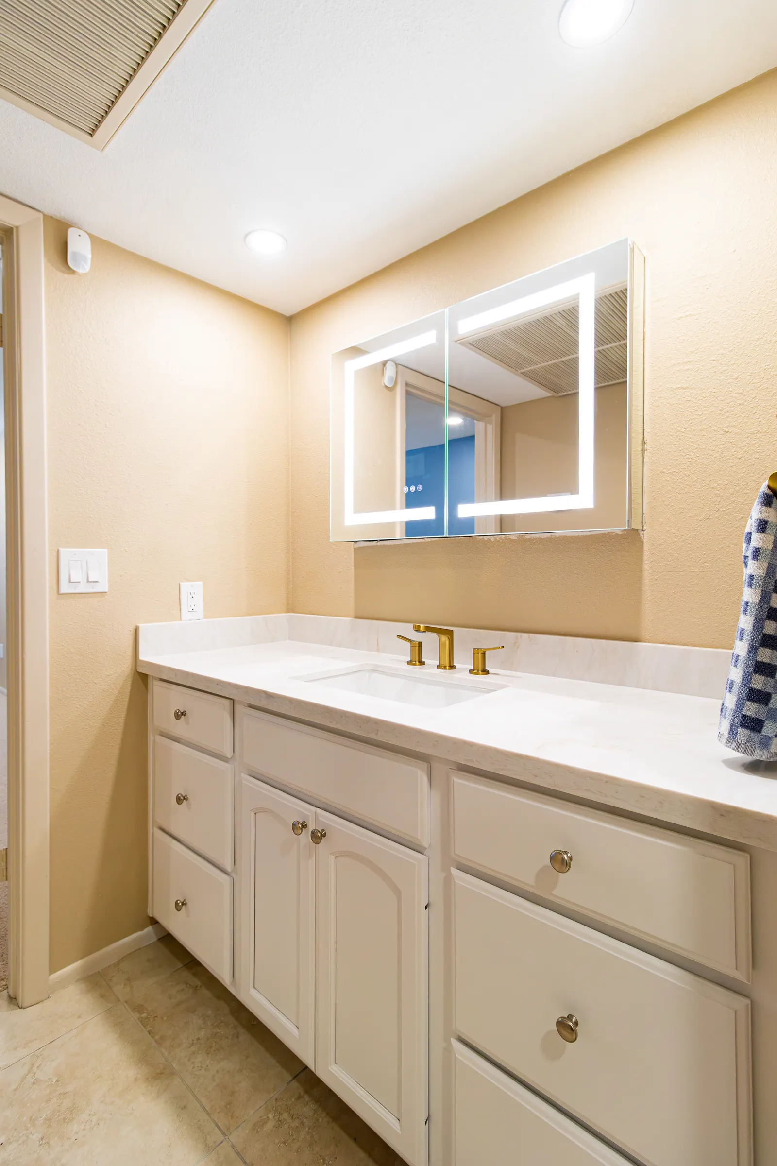 Second bathroom vanity in white cabinetry with a brass faucet and an LED-backlit mirror cabinet
