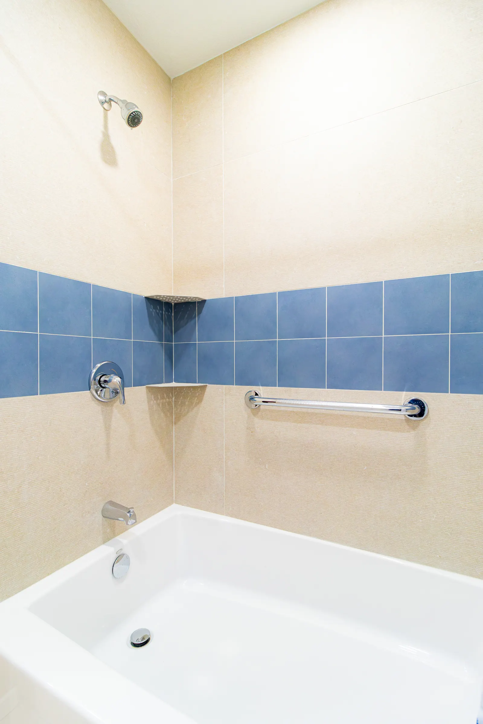 Alcove bathtub with a blue accent tile band and a horizontal grab bar mounted at the back wall