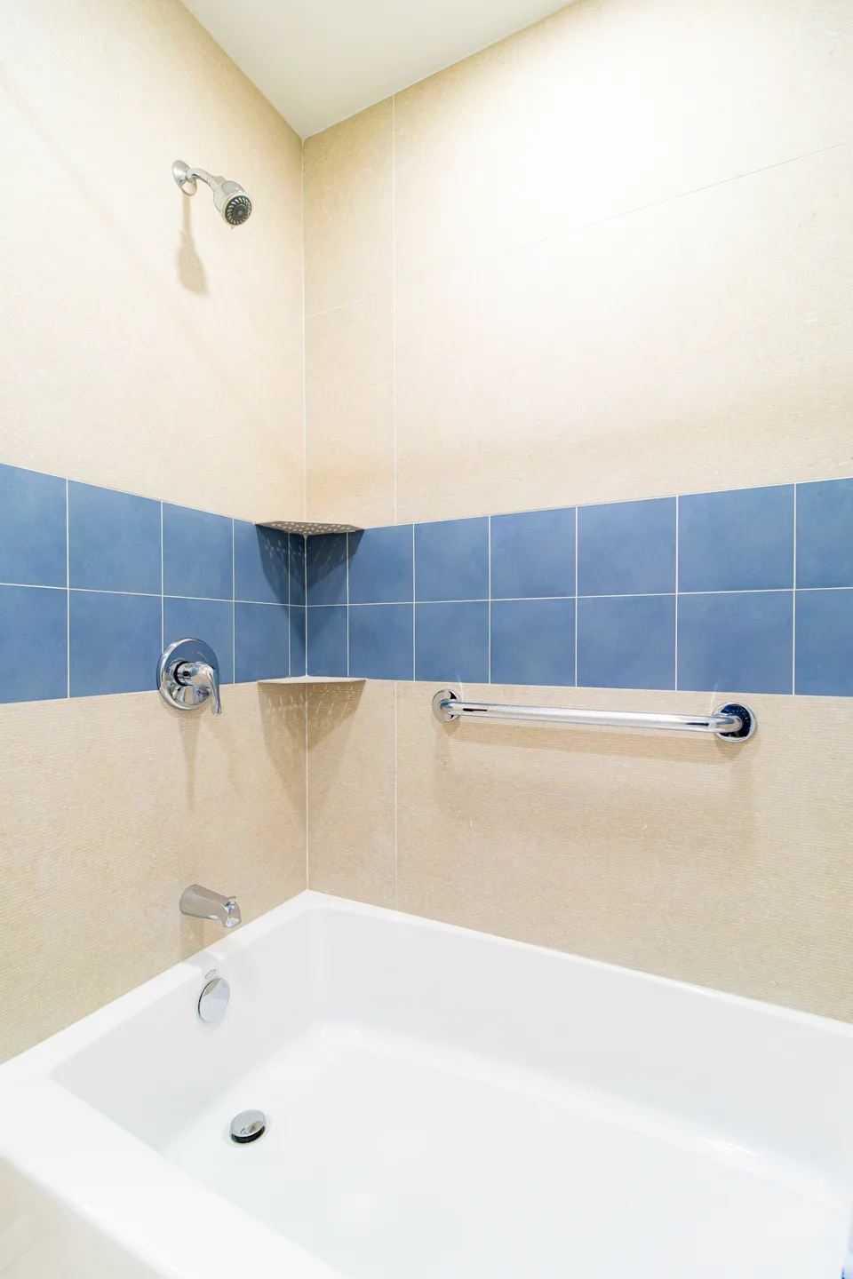 Alcove bathtub with a blue accent tile band and a grab bar