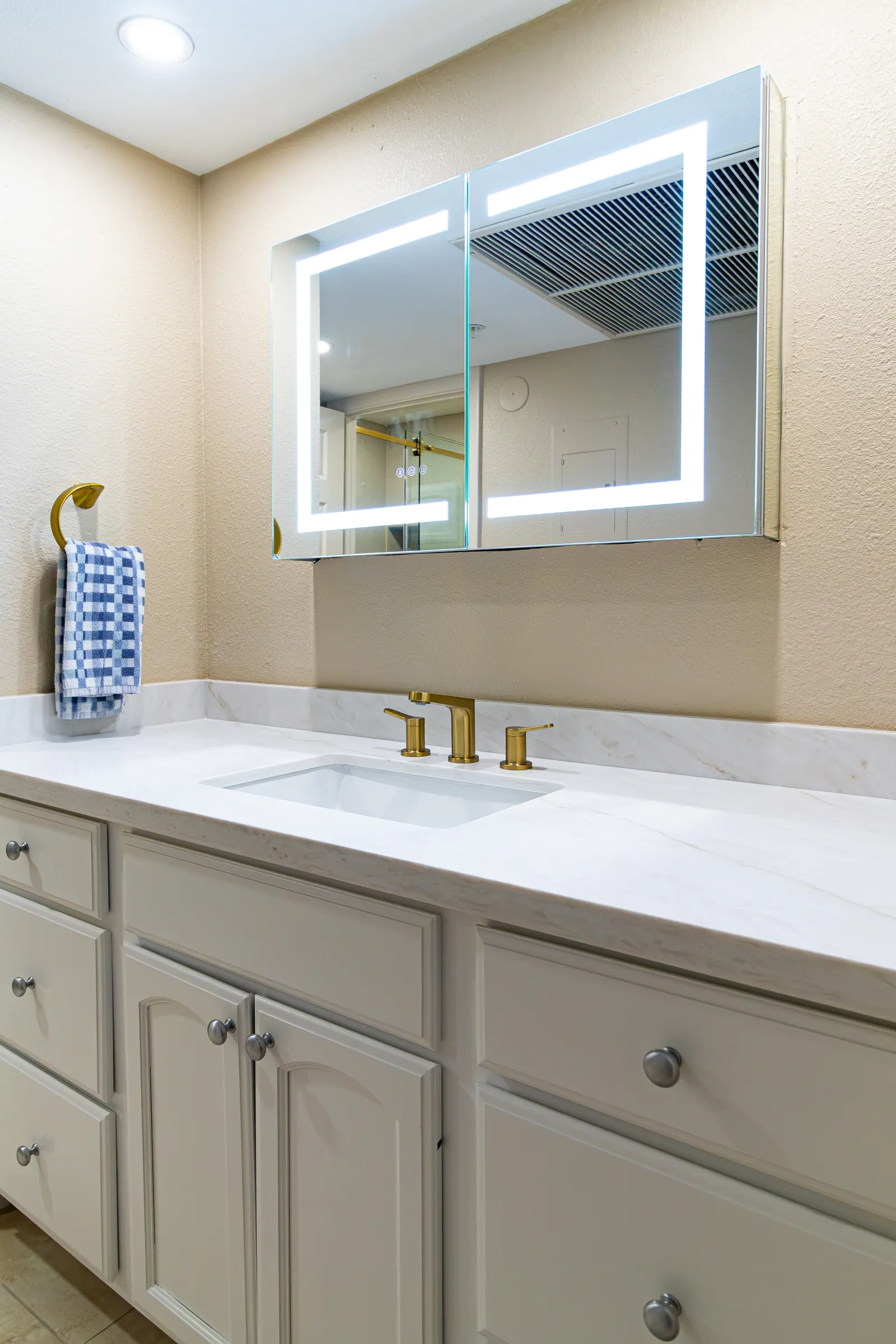 Full bathroom vanity in greige cabinetry with a marble-look top and an LED-backlit mirror cabinet