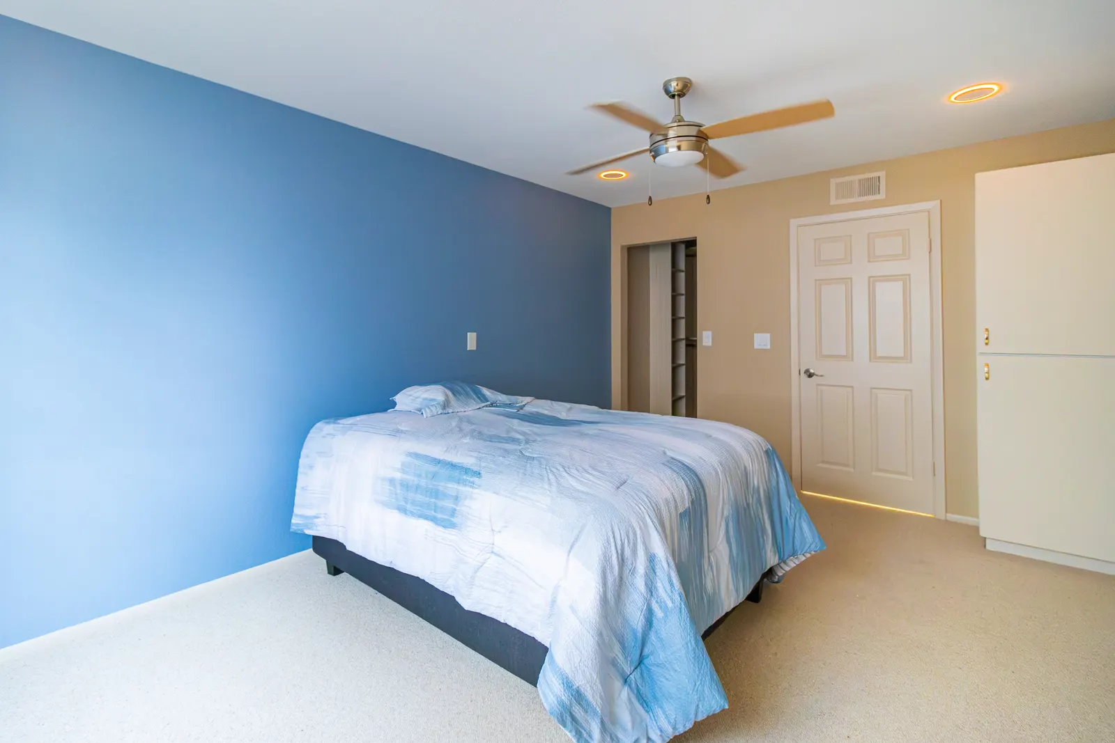 Bedroom with a deep blue accent wall behind the bed, a brushed nickel ceiling fan and pale carpet