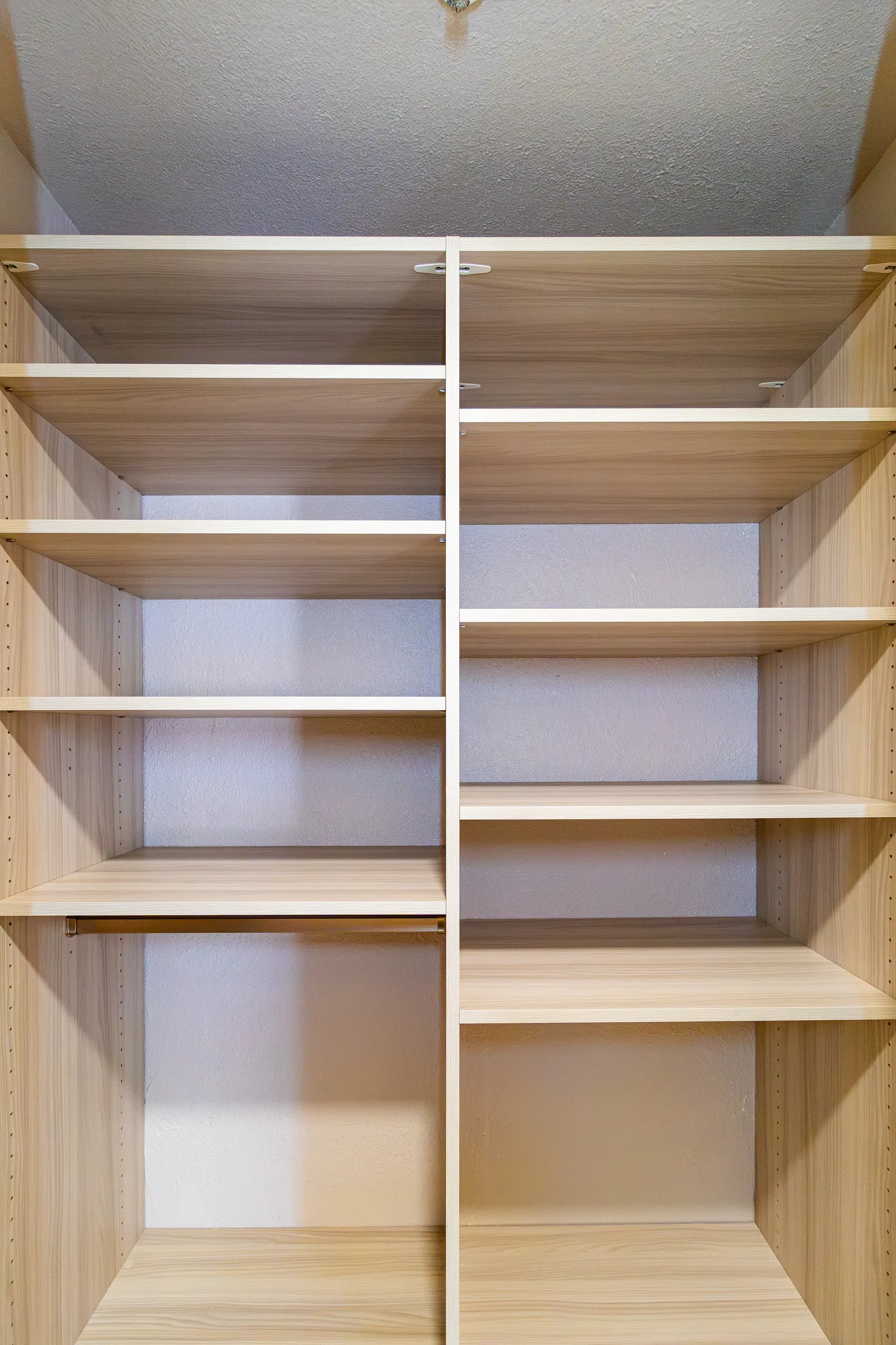 Reach-in closet built out in a light oak finish with adjustable shelves above a full-width hanging rod