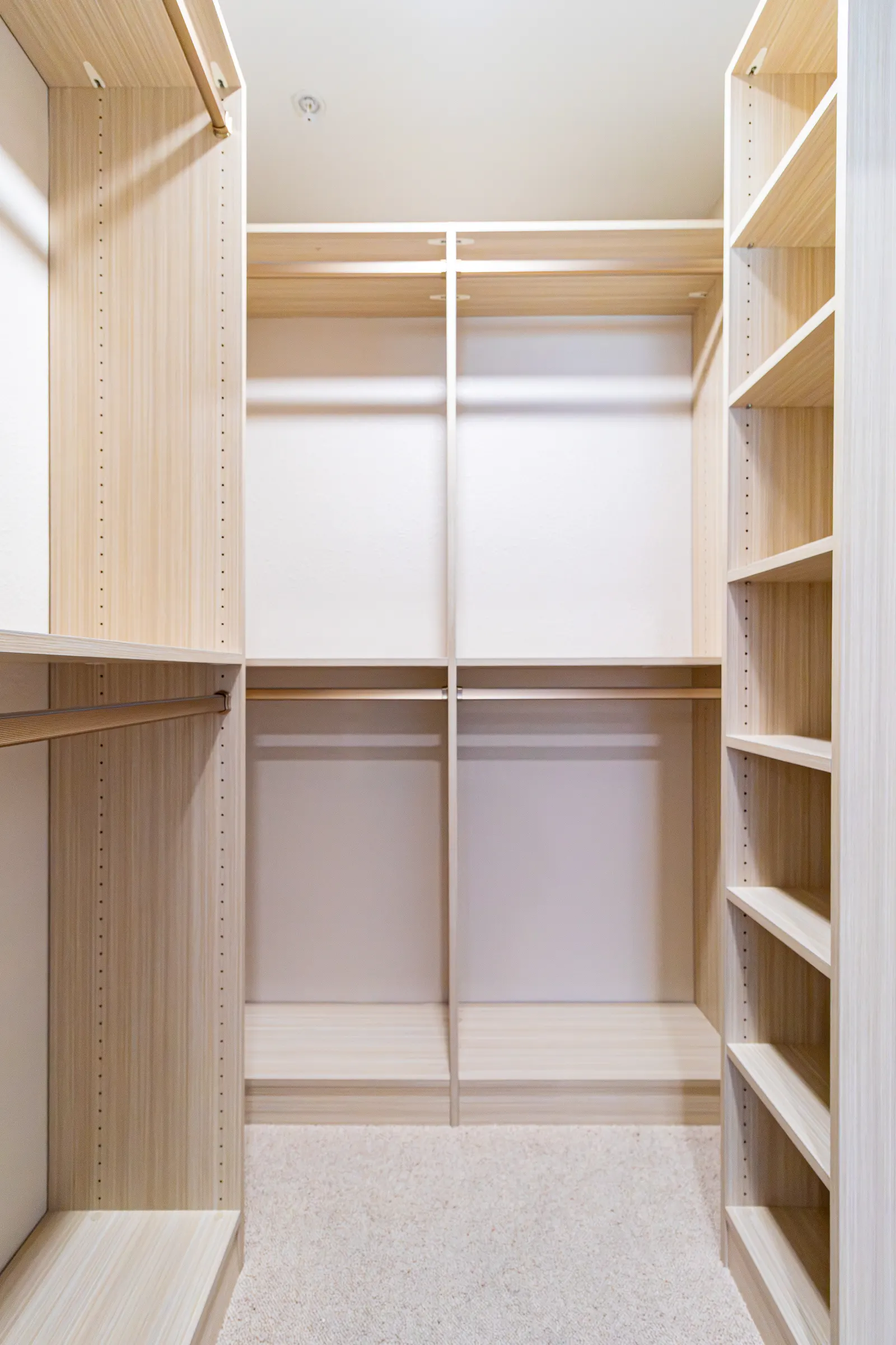 Light oak walk-in closet with corner shelf towers, upper hanging rods and a carpeted floor