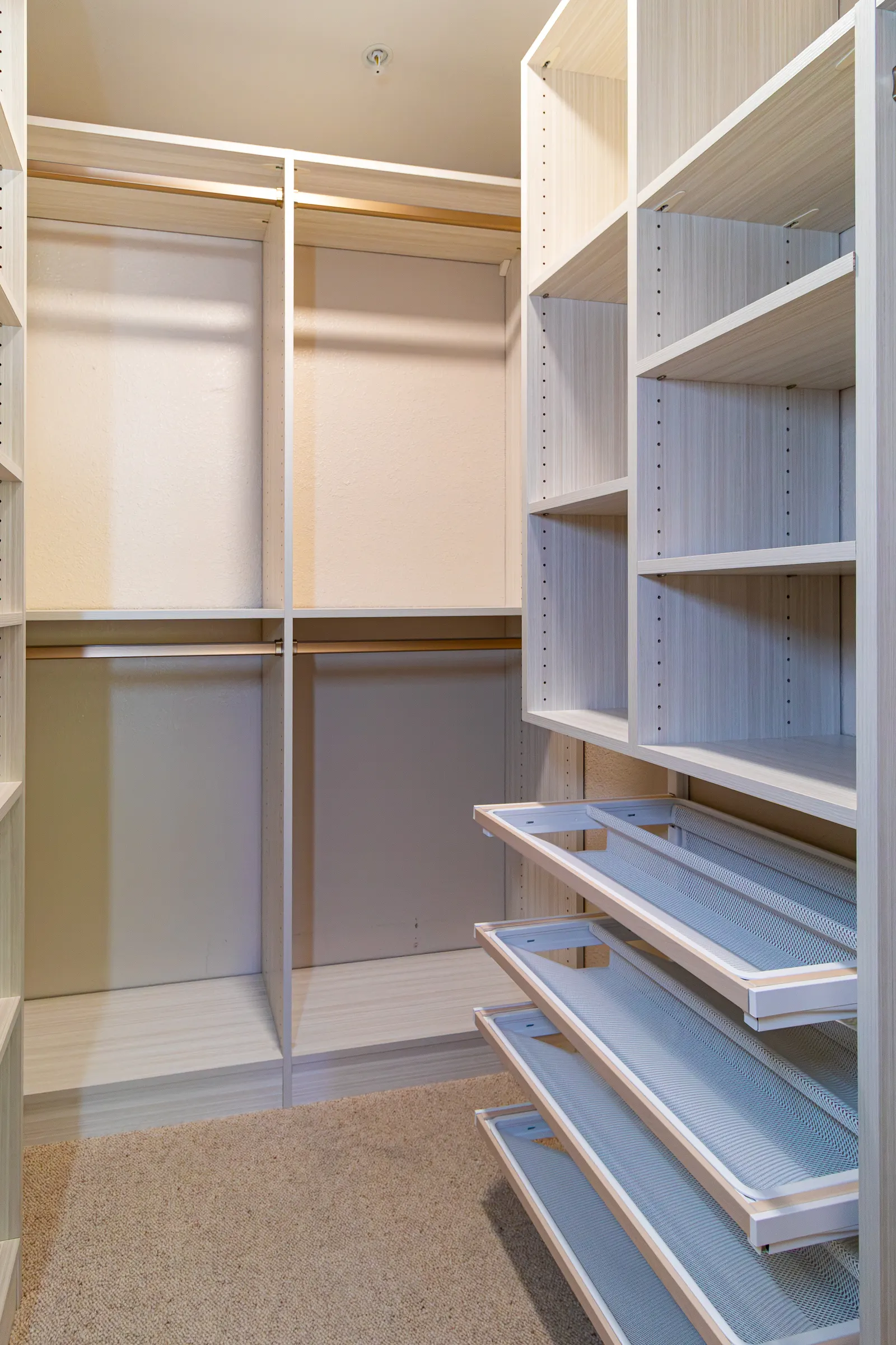 Custom walk-in closet in a pale finish with adjustable shelving, hanging rods and pull-out wire trays