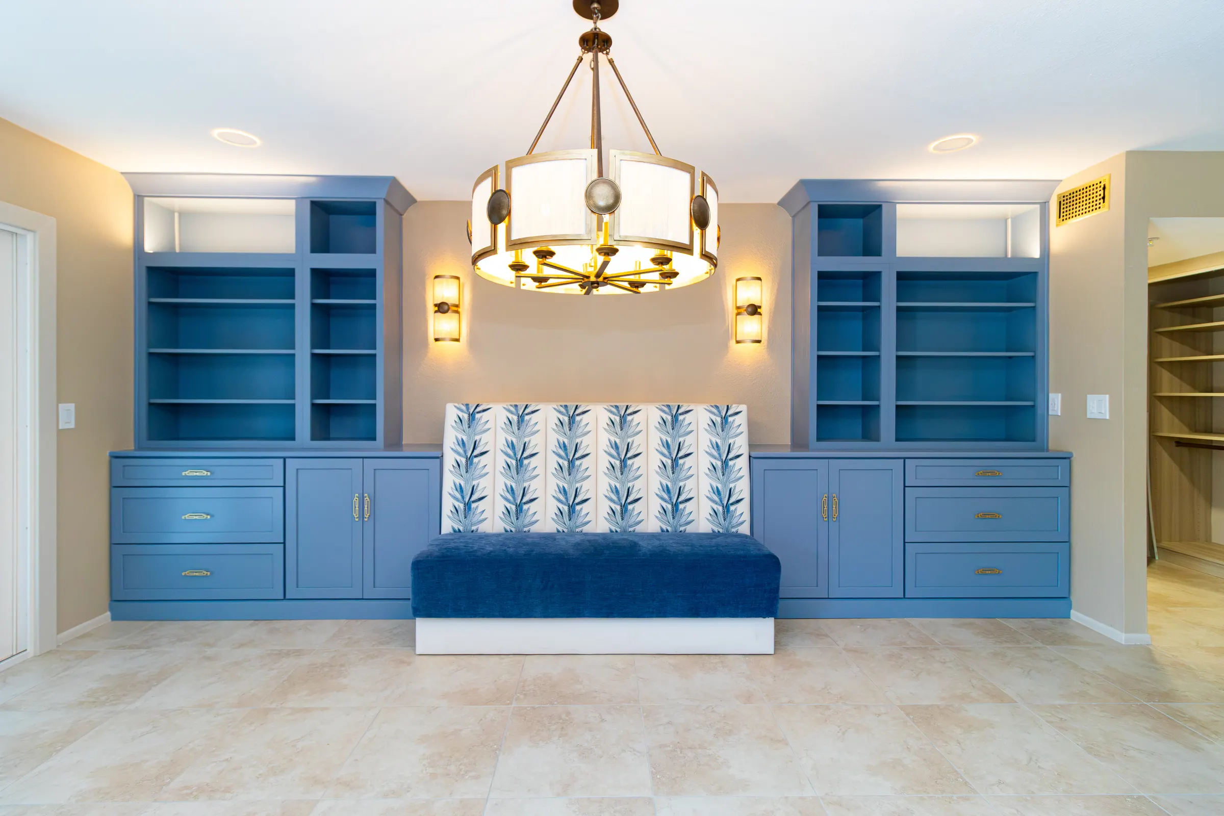 Great room with periwinkle-blue built-in cabinetry flanking an upholstered banquette in a blue botanical print, lit by a brass drum chandelier and two brass sconces