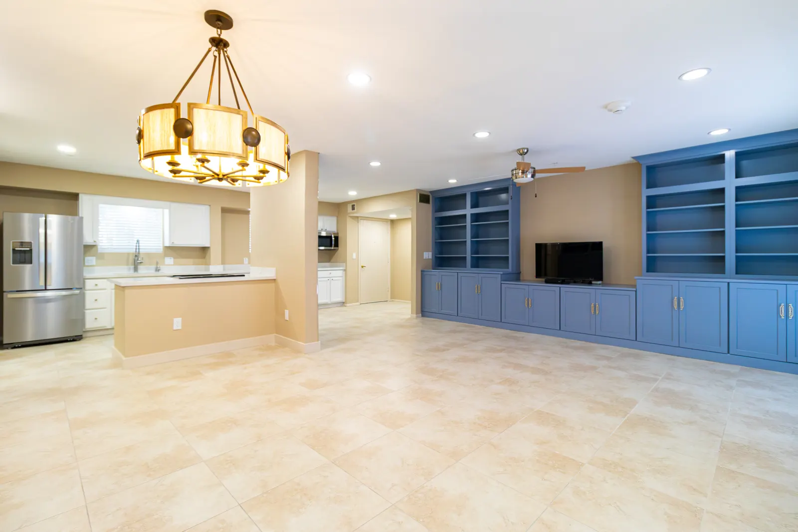 Kitchen island and stainless refrigerator in the foreground, opening to the great room and its brass chandelier
