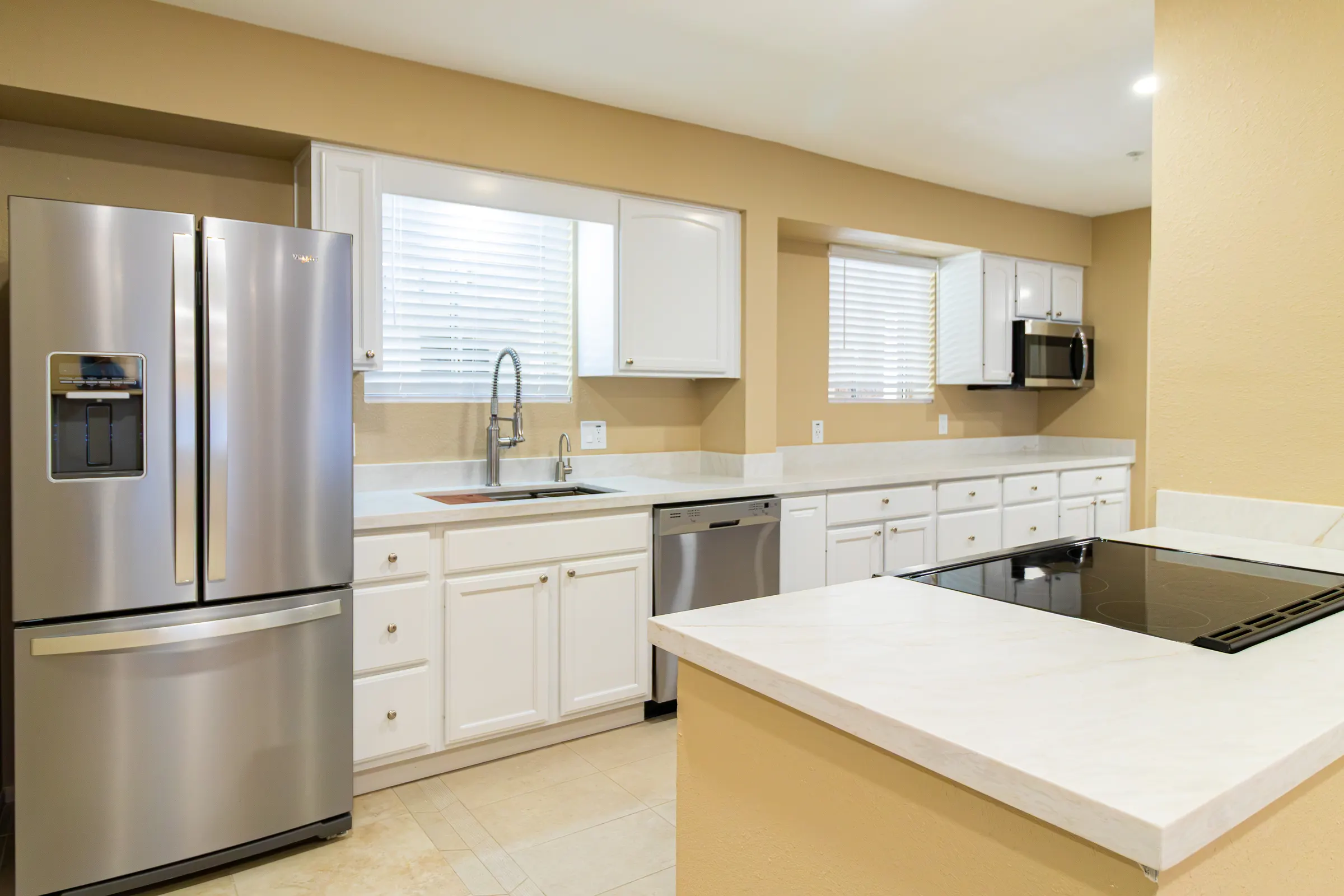 White shaker kitchen with quartz counters, stainless appliances and an island with a flush induction cooktop
